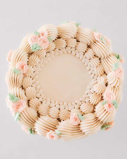 Top view of Charlotte cake showing a wreath of ruffled piping, beaded border, and pink roses with green leaves