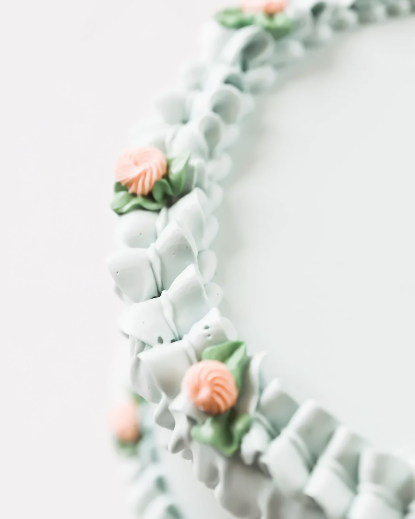 Close-up detail of Gail Marie's hand-piped mint green shell ruffle border with peach rosette blooms and sage green leaf clusters