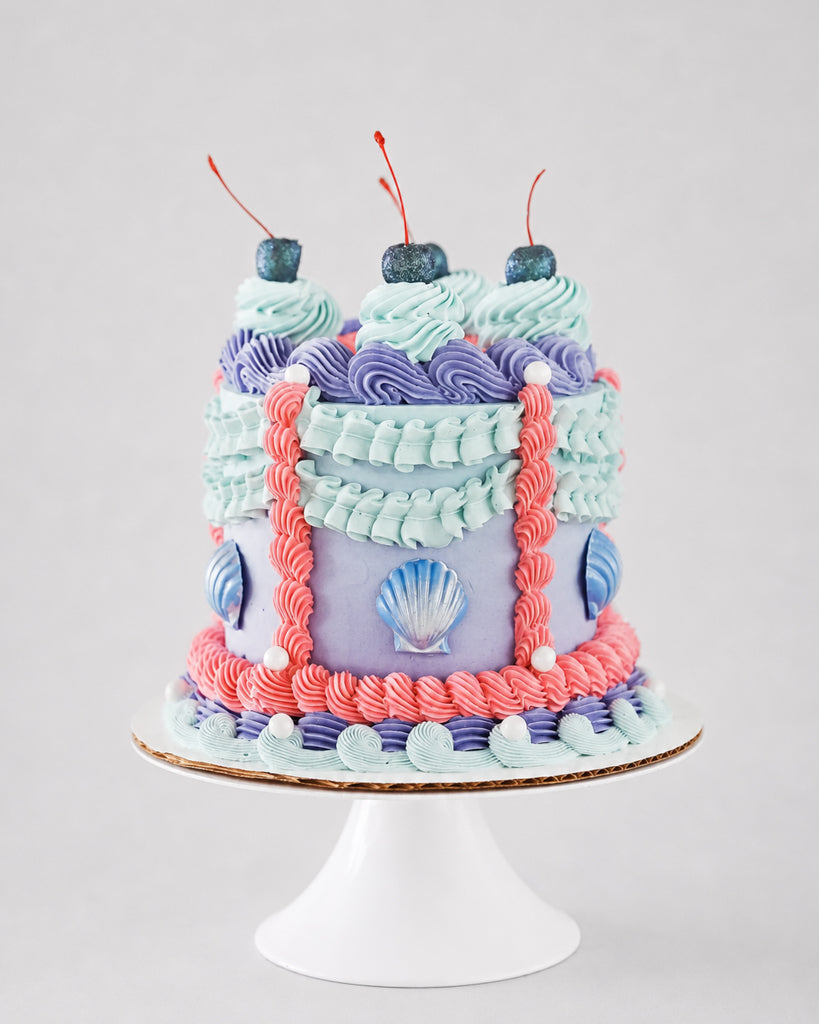 Ariel mermaid-themed cake with mint and lavender rosette wreath, glitter cherries, and coral ribbon piping