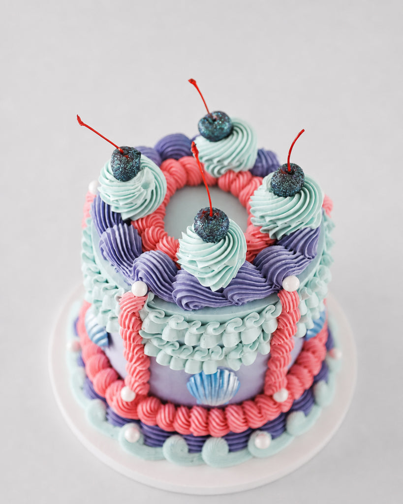 Ariel cake with lavender buttercream, chocolate seashells, coral ribbon stripes, and glitter cherry topper
