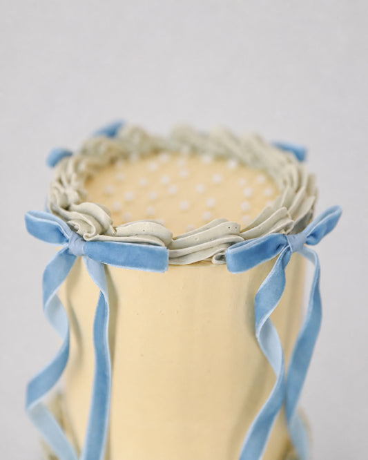 Top view of Bluebell Bow mini cake showing pearl dot sprinkles, shell piping border, and velvet bow