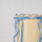 Close-up of Bluebell Bow mini cake showing pearl dot sprinkles, pale blue shell piping, and velvet ribbon bows