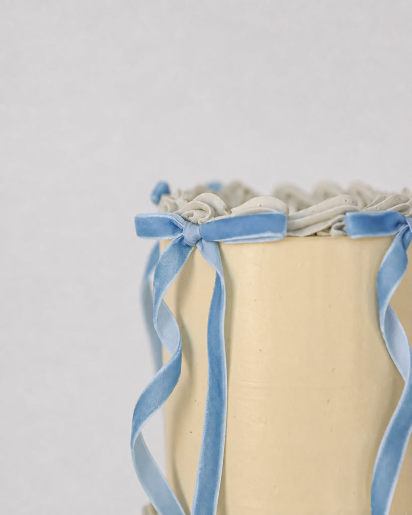 Close-up of Bluebell Bow mini cake showing pearl dot sprinkles, pale blue shell piping, and velvet ribbon bows