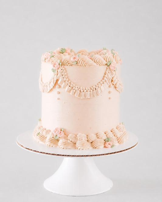 Charlotte vintage cake in soft blush with beaded pearl garland, ruffled piping, and pink rose accents