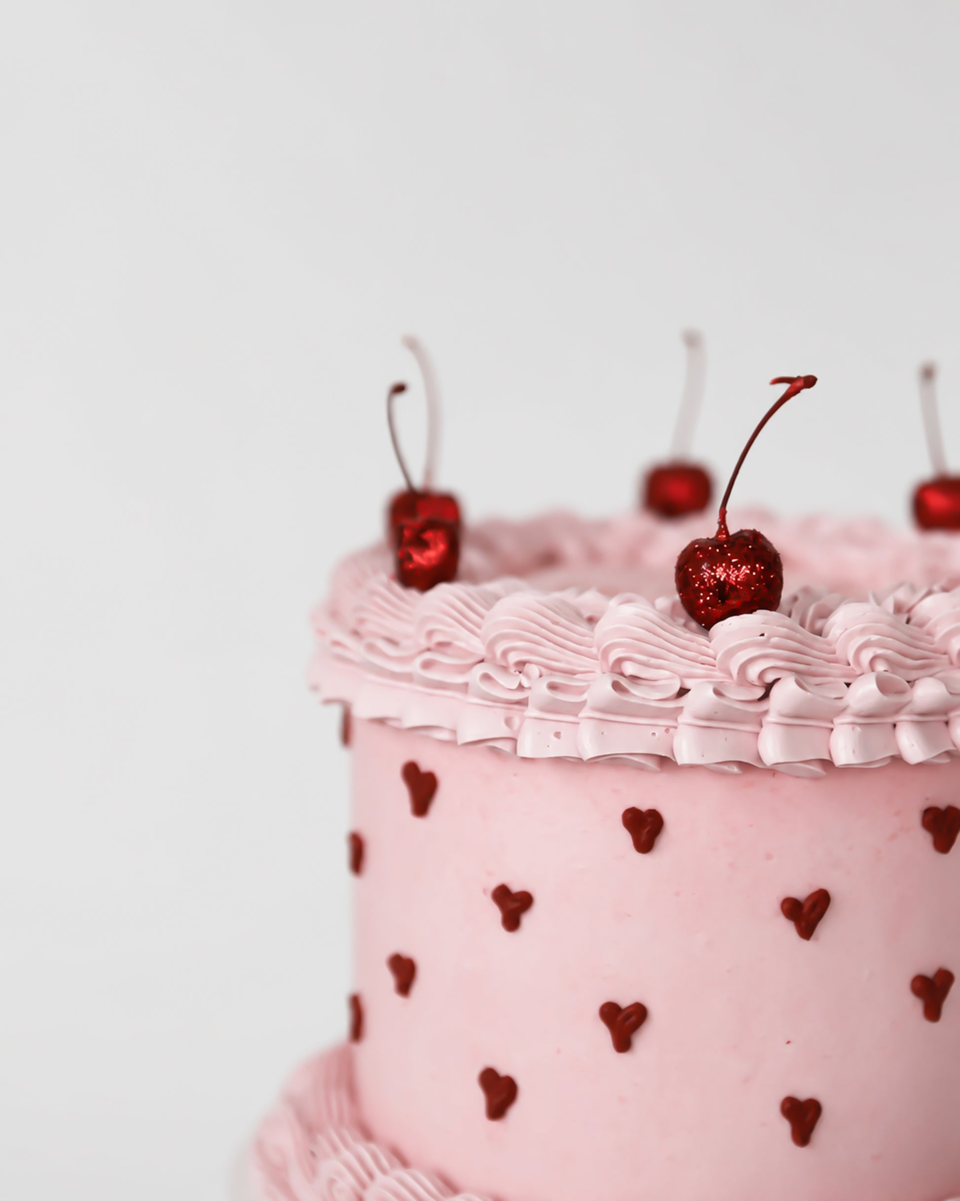 Close-up of blush pink buttercream cake with hand-piped dark red heart dot pattern