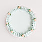 Top-down view of Gail Marie cake showing smooth pale mint green buttercream center surrounded by a hand-piped ruffle border with peach rosettes and sage leaf accents