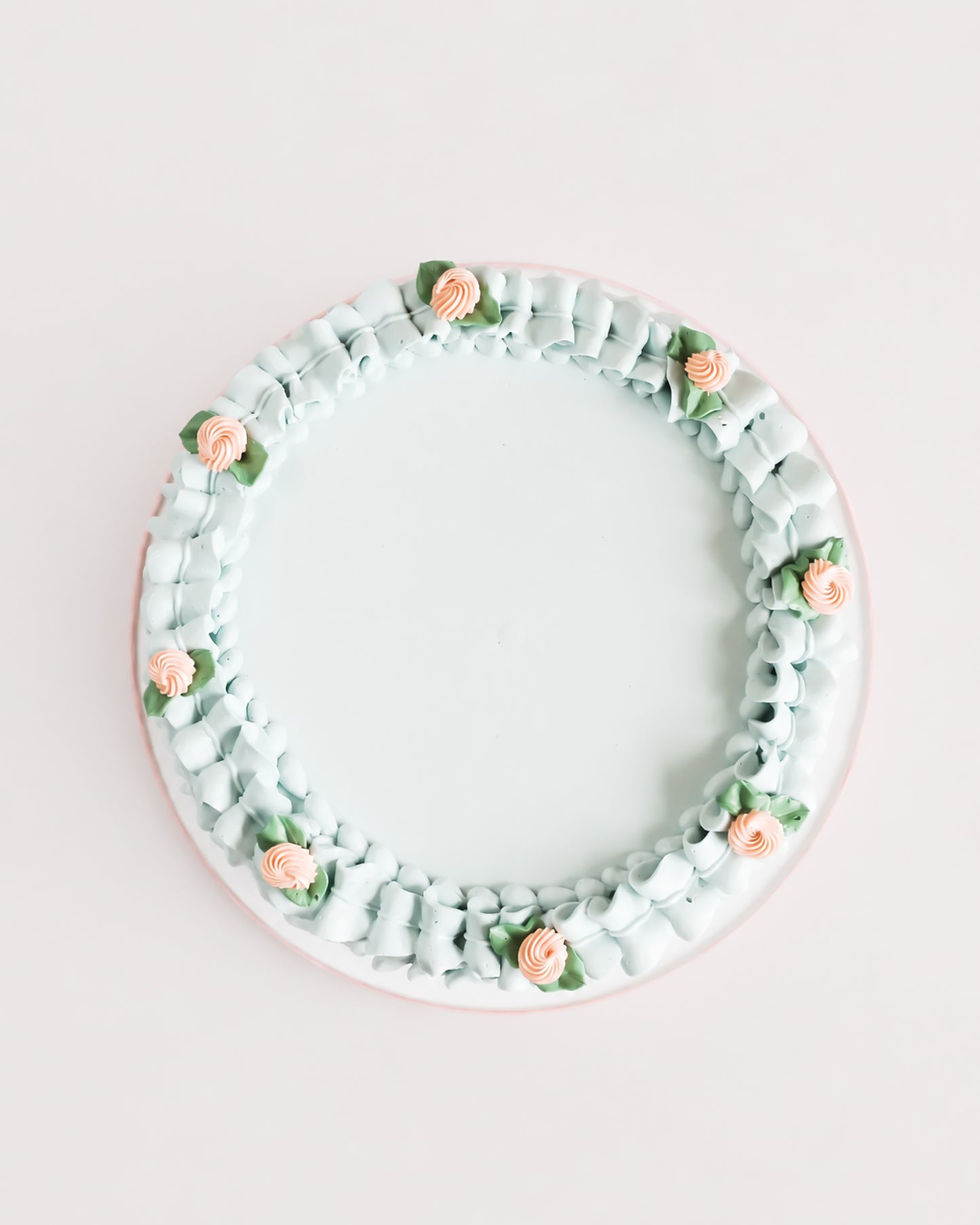 Top-down view of Gail Marie cake showing smooth pale mint green buttercream center surrounded by a hand-piped ruffle border with peach rosettes and sage leaf accents