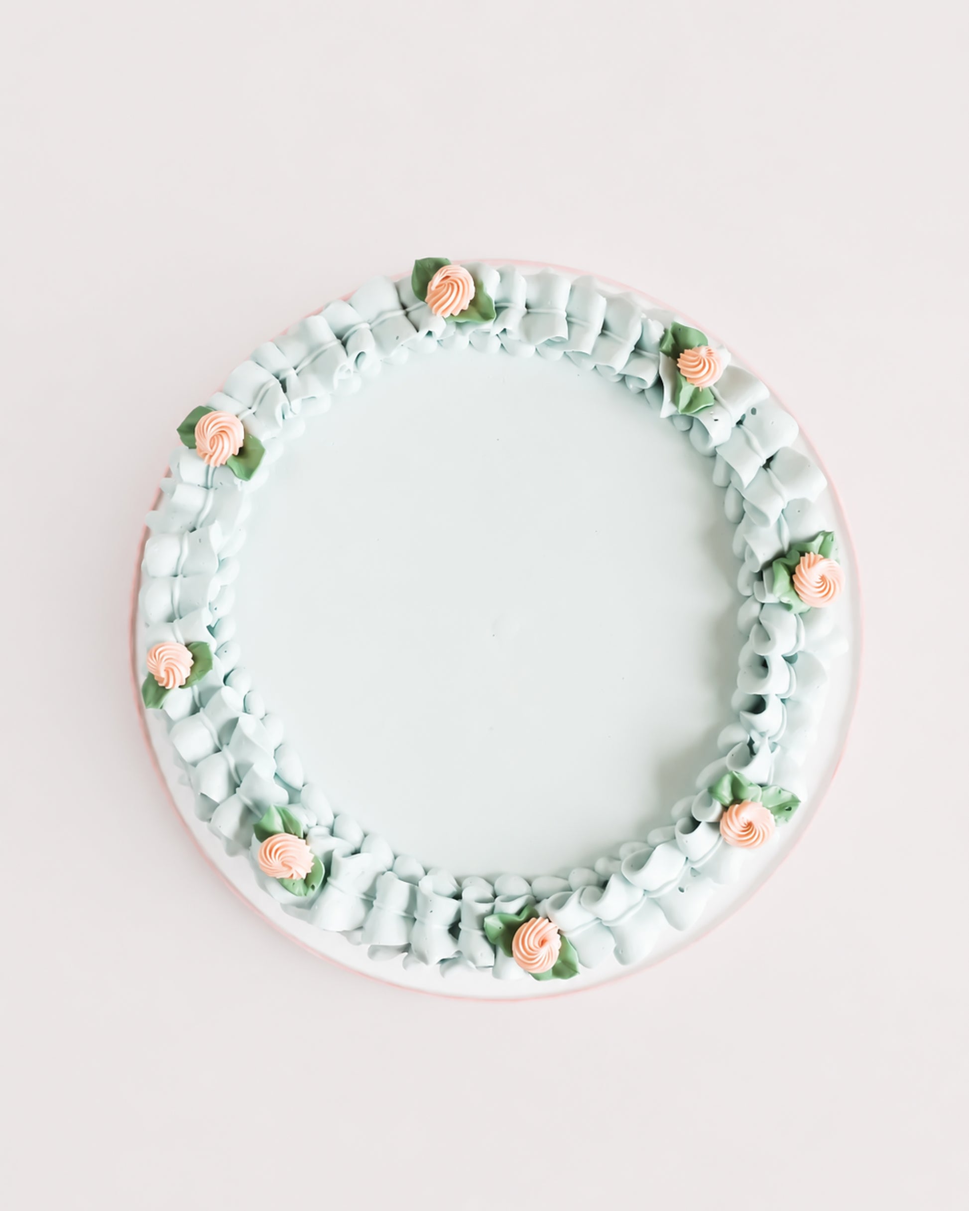 Top-down view of Gail Marie cake showing smooth pale mint green buttercream center surrounded by a hand-piped ruffle border with peach rosettes and sage leaf accents