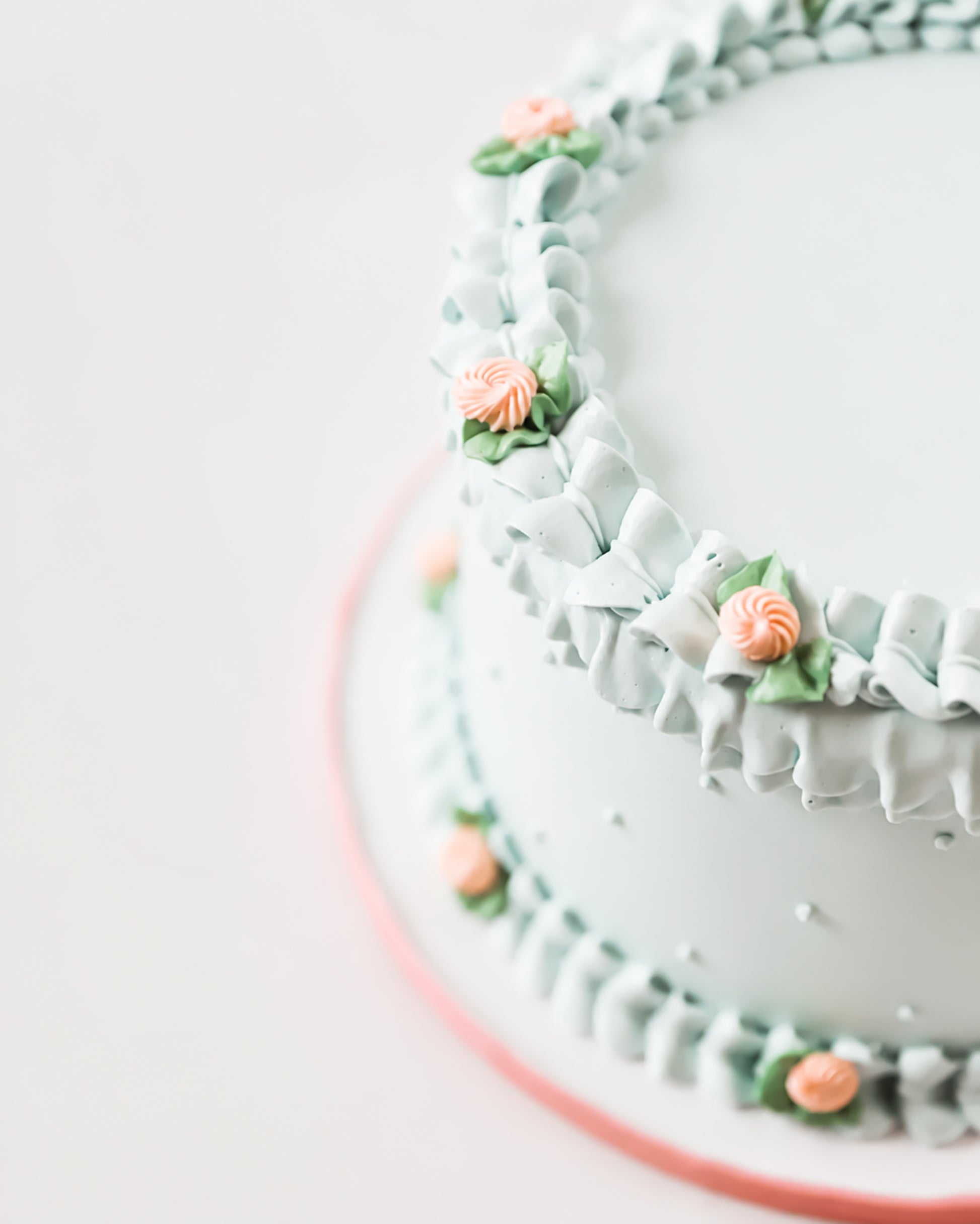 Angled close-up of Gail Marie cake showing smooth mint green sides with pearl dot details and hand-piped ruffle borders accented with peach rosettes and sage leaves