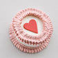 Mini snack cake in pink with a red heart accent and ruffled piped border