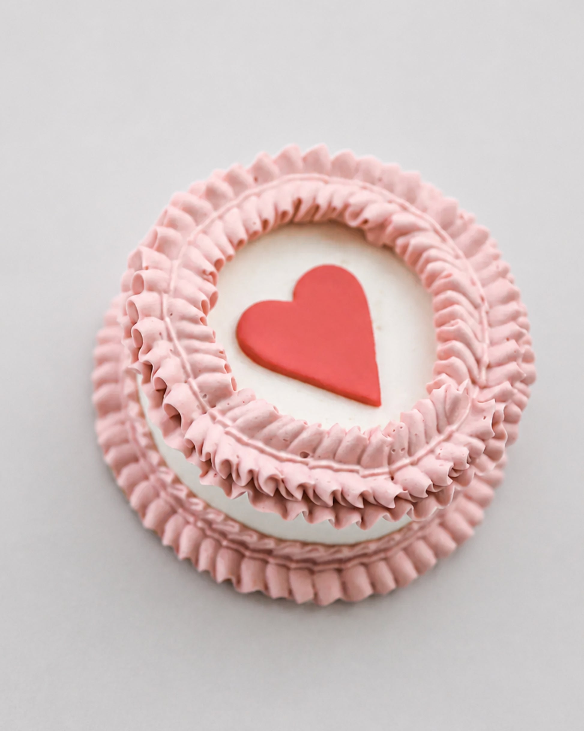 Mini snack cake in pink with a red heart accent and ruffled piped border