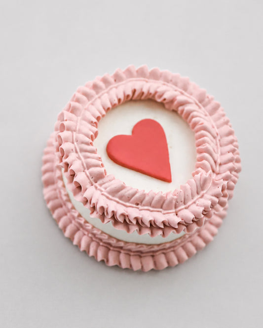 Mini snack cake in pink with a red heart accent and ruffled piped border