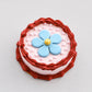 Mini snack cake in pink with a red ruffled border, blue flower, and pink pearls