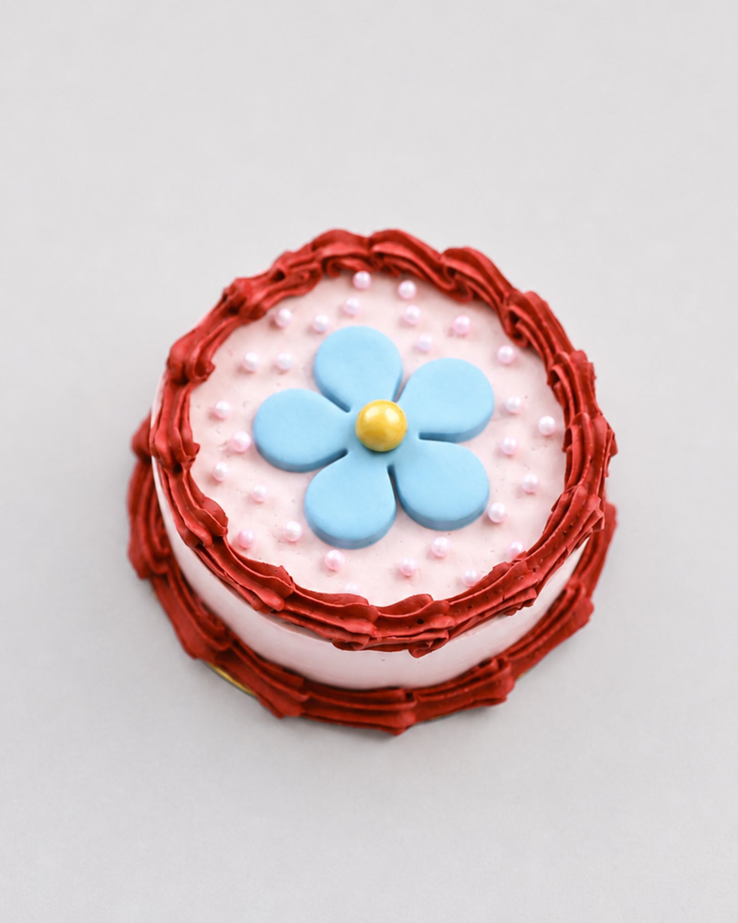 Mini snack cake in pink with a red ruffled border, blue flower, and pink pearls