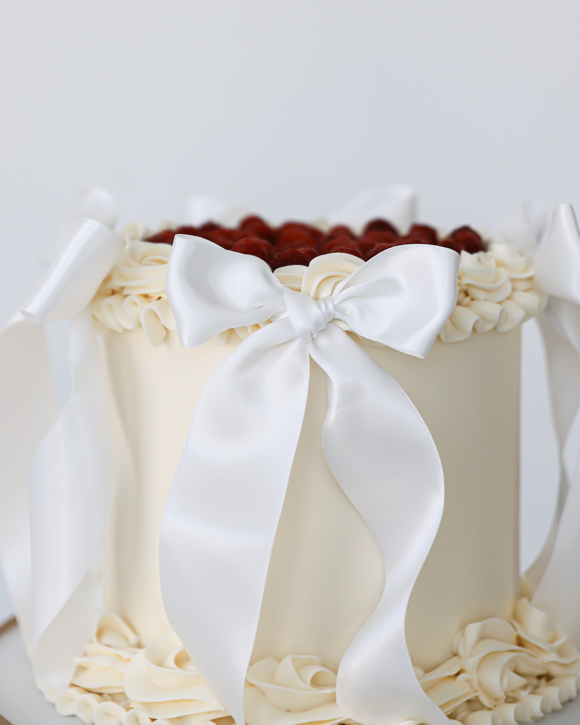 Close-up of white bow detail on buttercream cake with raspberries