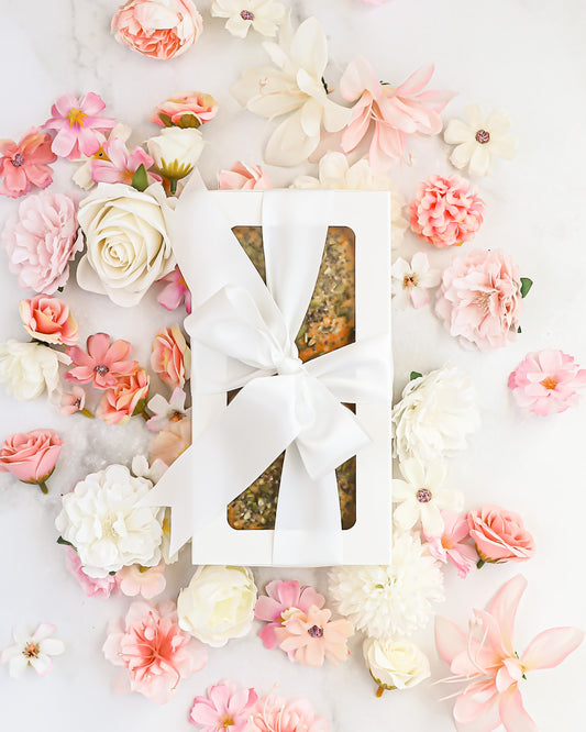 Gift box with seeded cake tied with white ribbon and pastel flowers