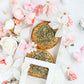 Open gift box revealing mini cakes topped with seeds and florals