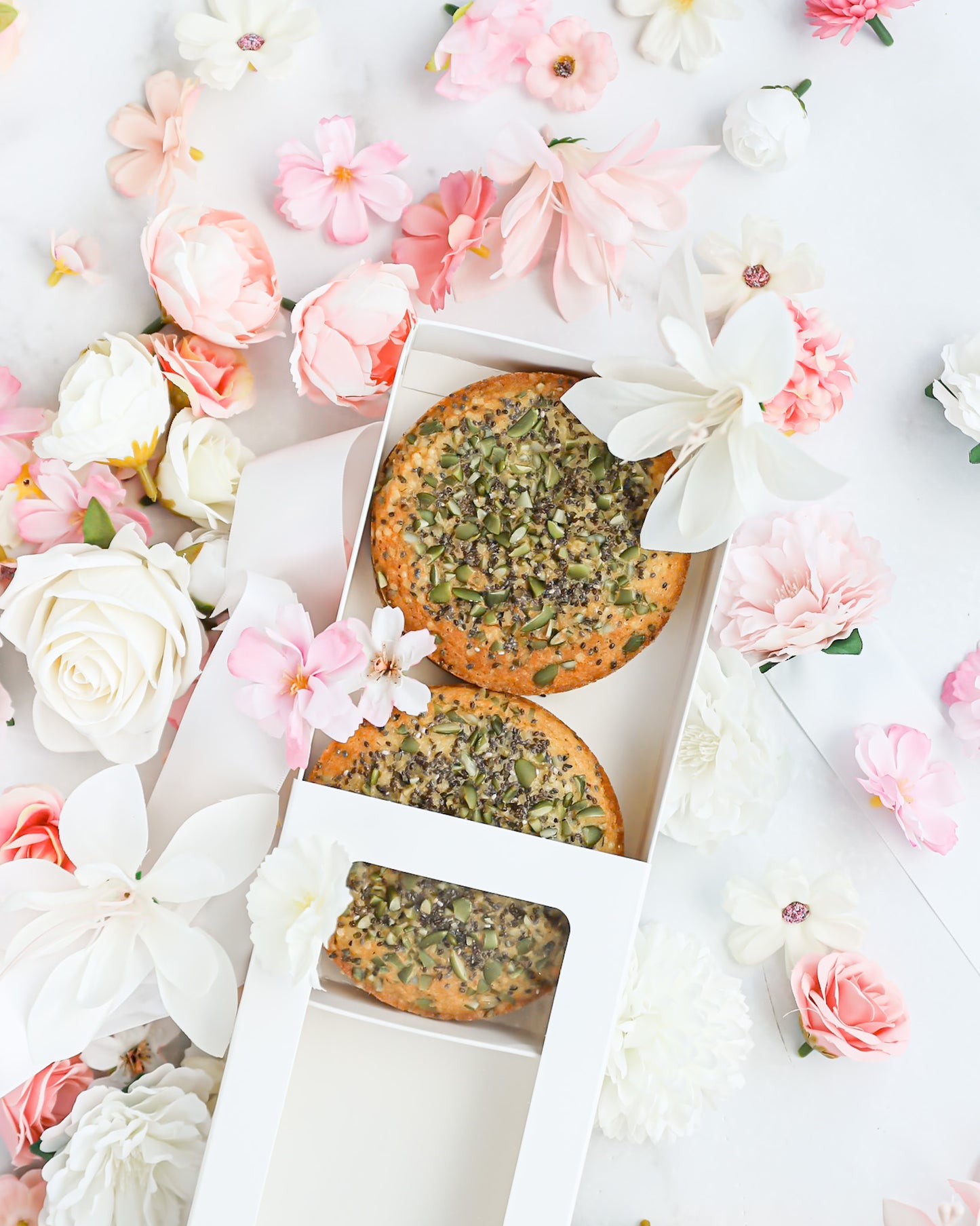 Open gift box revealing mini cakes topped with seeds and florals