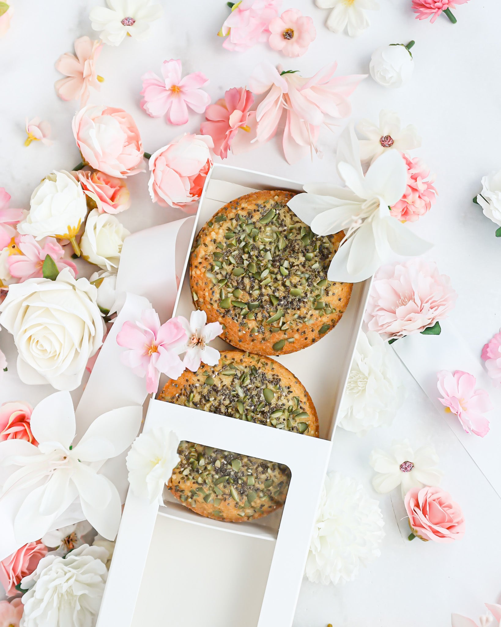 Open gift box revealing mini cakes topped with seeds and florals