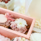 Close-up of buttercream cakelet with edible flower and macaron in pink box