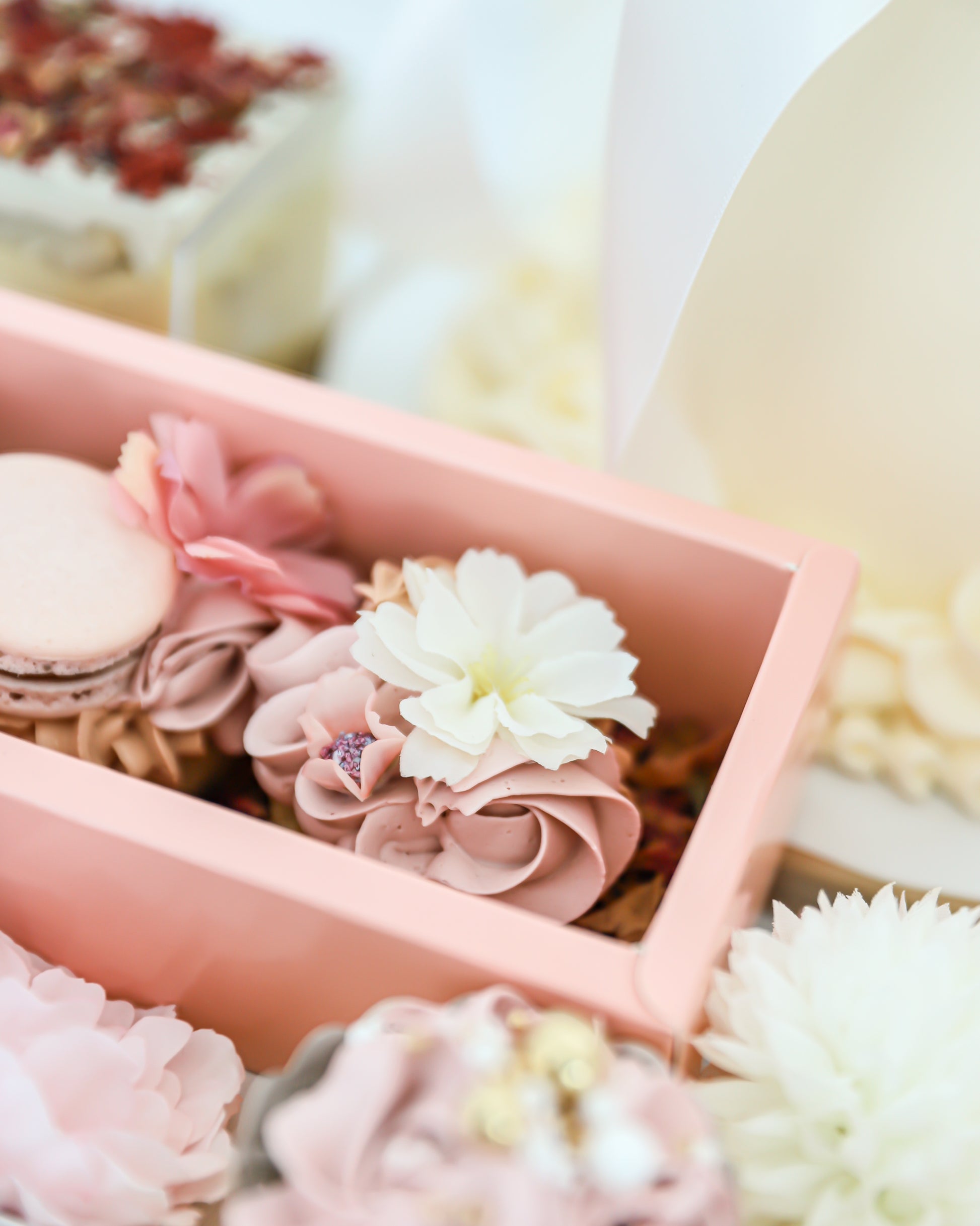 Close-up of buttercream cakelet with edible flower and macaron in pink box