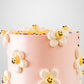 Close-up of blush pink buttercream cake with scattered white piped daisy flowers with yellow smiley face centers