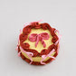 Mini snack cake in yellow with maroon piped rosettes and a pink bow