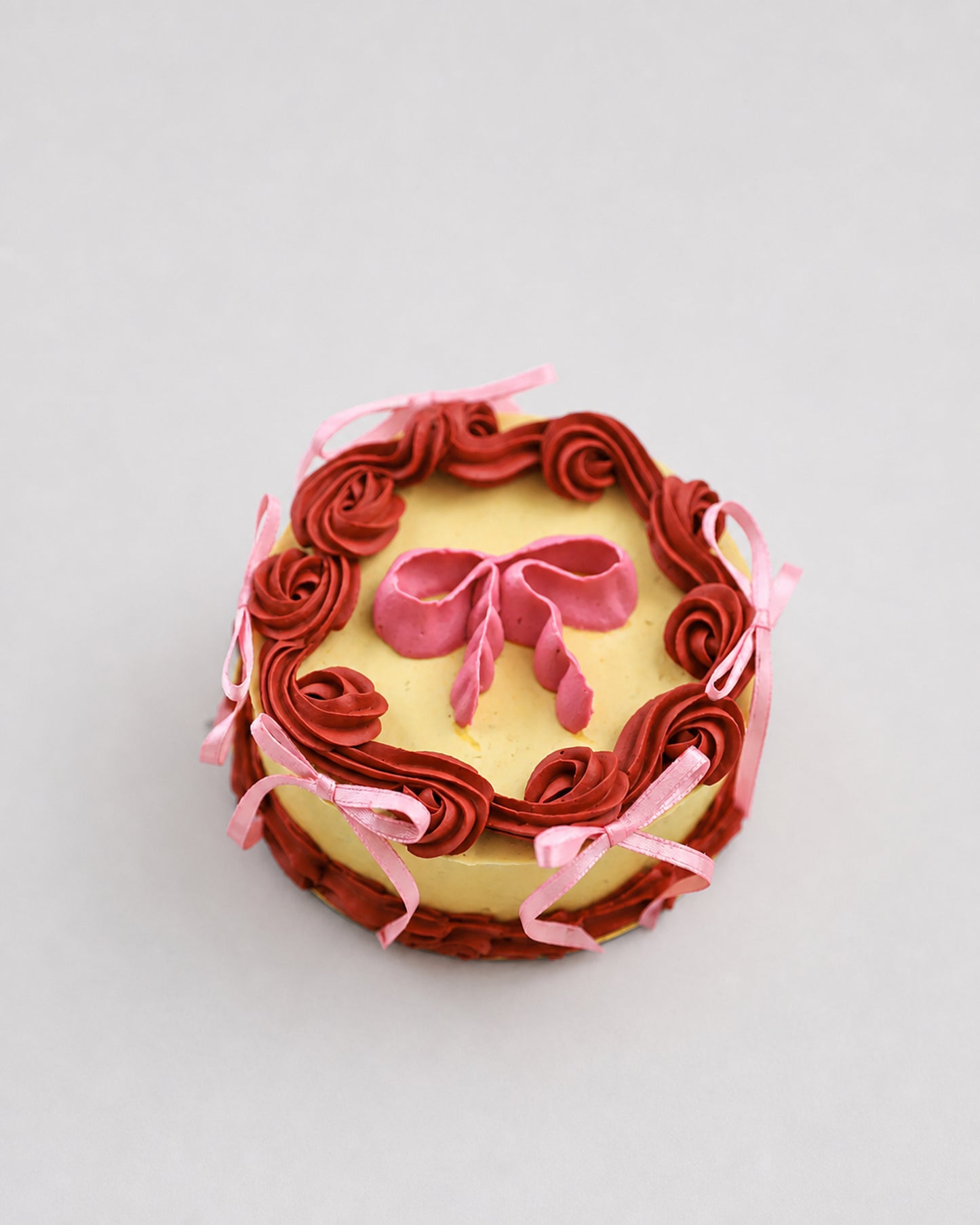 Mini snack cake in yellow with maroon piped rosettes and a pink bow