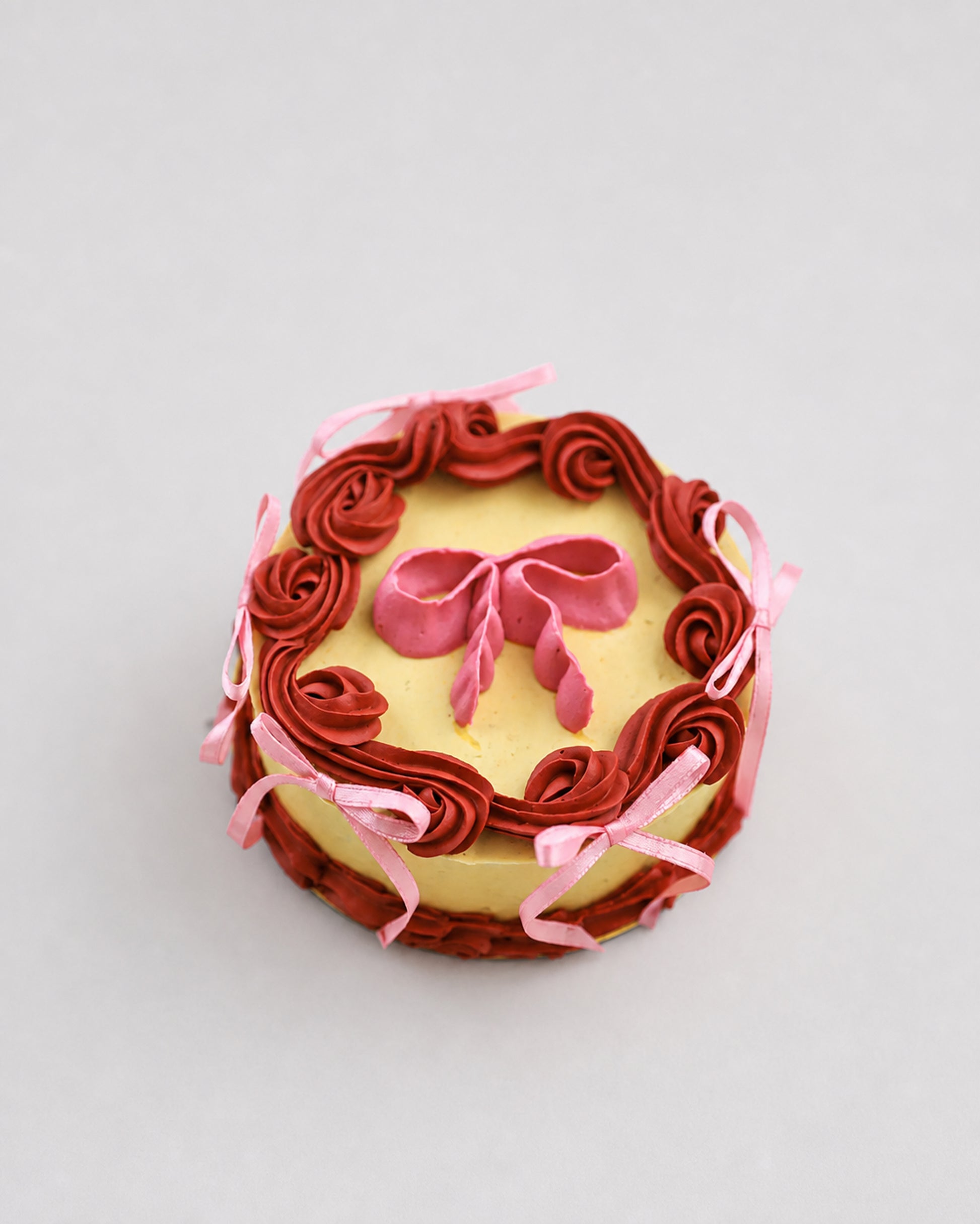 Mini snack cake in yellow with maroon piped rosettes and a pink bow