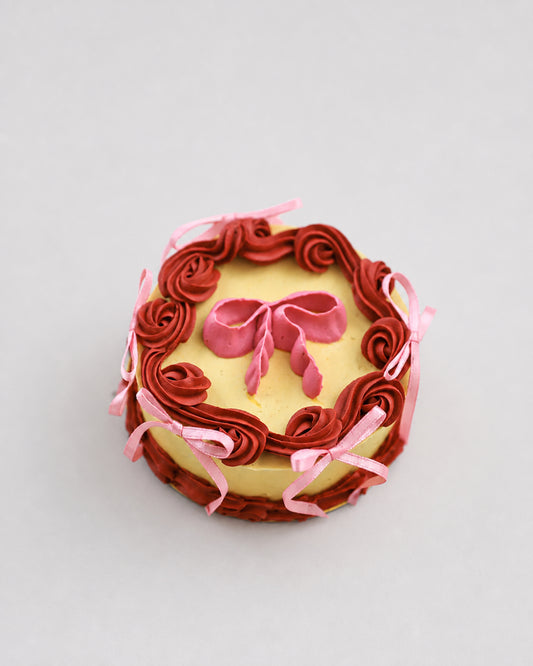 Mini snack cake in yellow with maroon piped rosettes and a pink bow