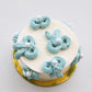 Mini snack cake in cream with teal piped swirls, pearls, and gold accents