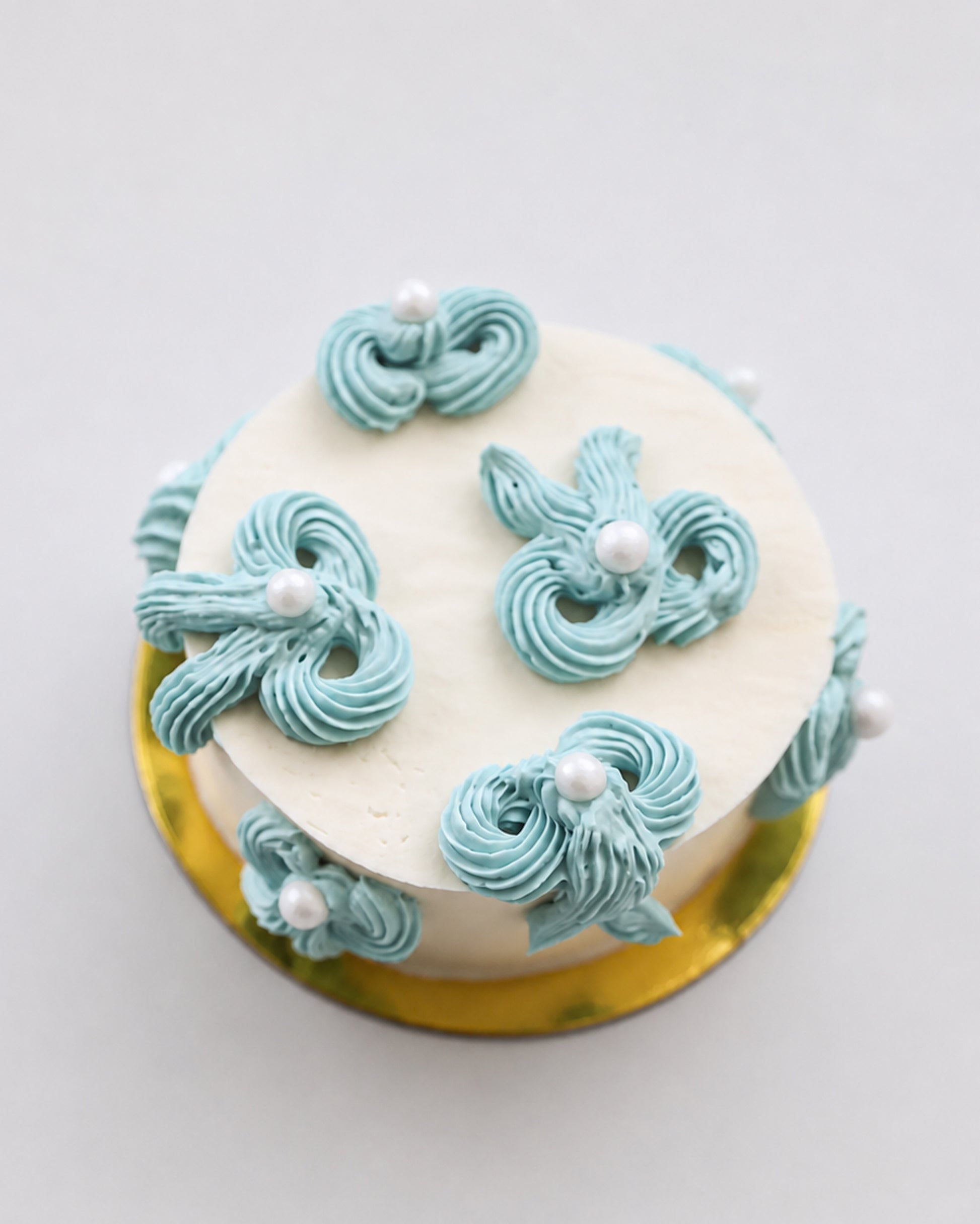 Mini snack cake in cream with teal piped swirls, pearls, and gold accents