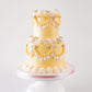 Two-tier butter yellow vintage buttercream cake with golden piped swags, white ruffle fan borders, and blush pink rosettes on a white cake stand