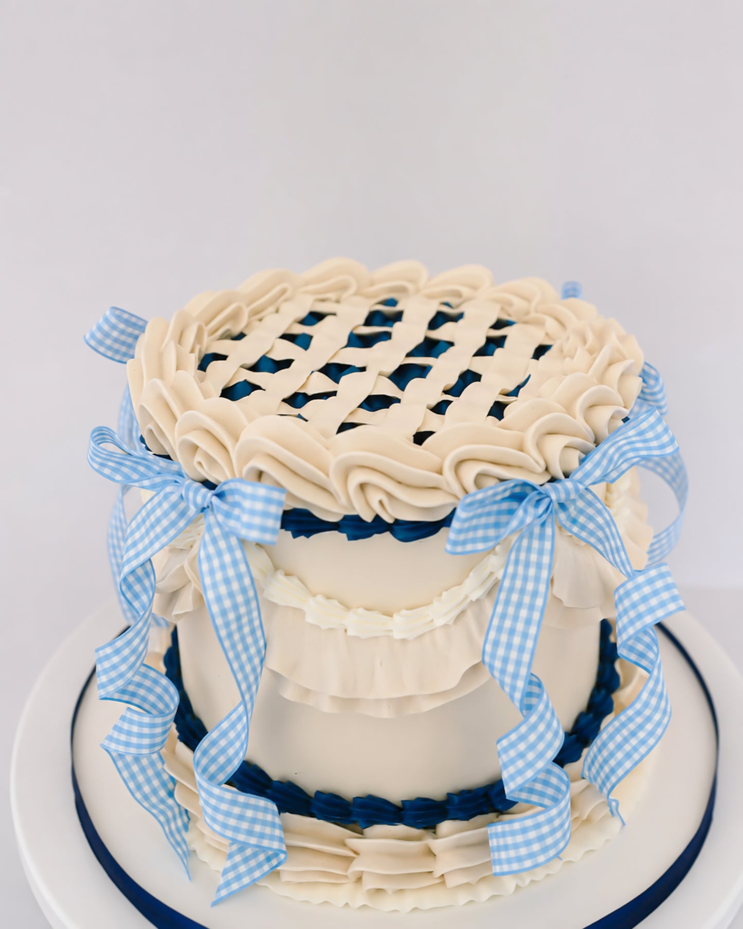 Top view of Sweetie Pie vintage lattice cake showing cream buttercream lattice top, crimped crown edge, and blue gingham ribbon