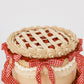 Close-up of Sweetie Pie cherry cake showing hand-piped buttercream lattice top and crimped crown edge with red cherry filling