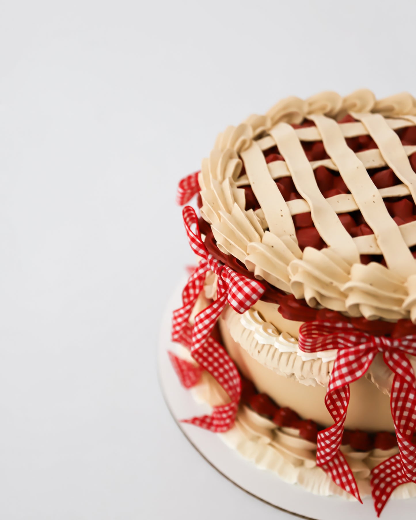 Angled view of Sweetie Pie cherry vintage lattice cake with red gingham ribbon bows and golden buttercream ruffles