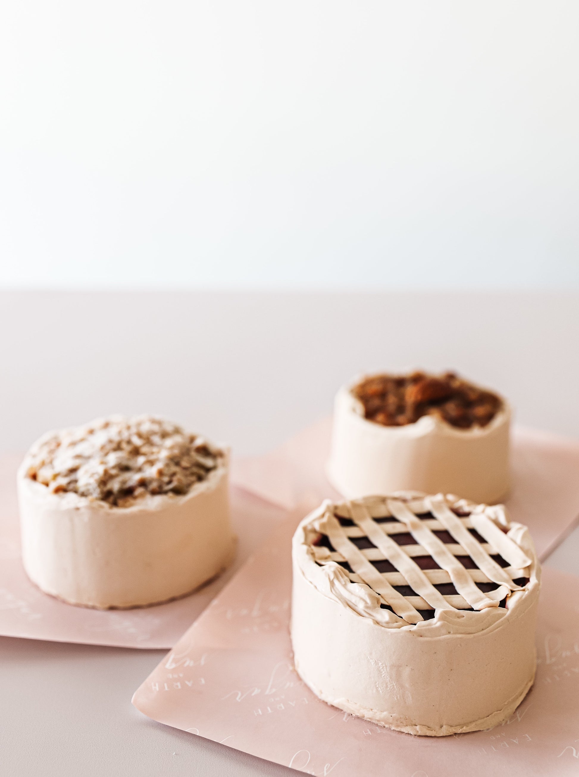 Three Thanksgiving-inspired cakes: one designed as an apple crumble pie, another with a classic lattice top, and the third boasting a pecan caramel finish.